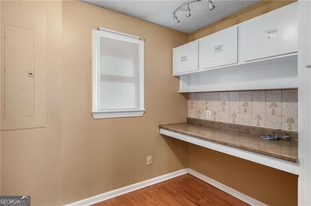 kitchen featuring electric panel, light hardwood / wood-style floors, decorative backsplash, and a textured ceiling