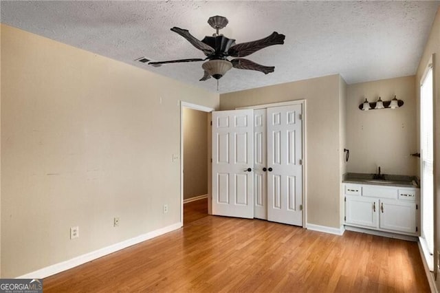 unfurnished bedroom with sink, a textured ceiling, ceiling fan, and light hardwood / wood-style flooring