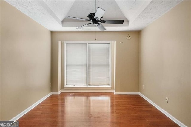 empty room with hardwood / wood-style flooring, a raised ceiling, and a textured ceiling