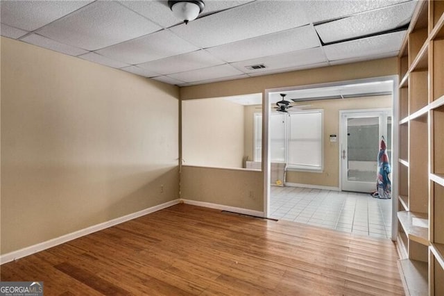 basement featuring wood-type flooring, a drop ceiling, and ceiling fan