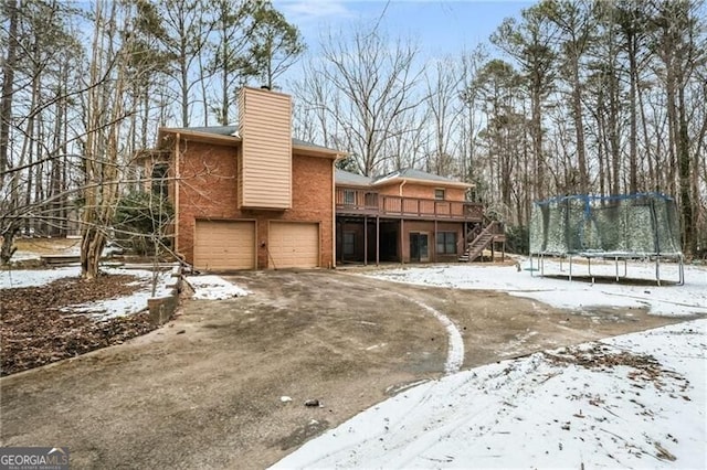 snow covered back of property featuring a garage, a wooden deck, and a trampoline