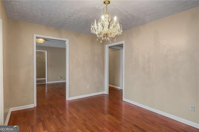 spare room featuring dark wood-type flooring, a chandelier, and a textured ceiling