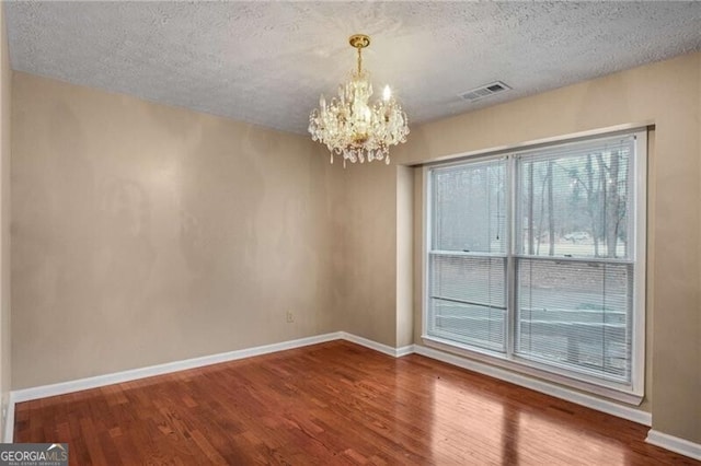 empty room featuring wood-type flooring, a chandelier, and a textured ceiling