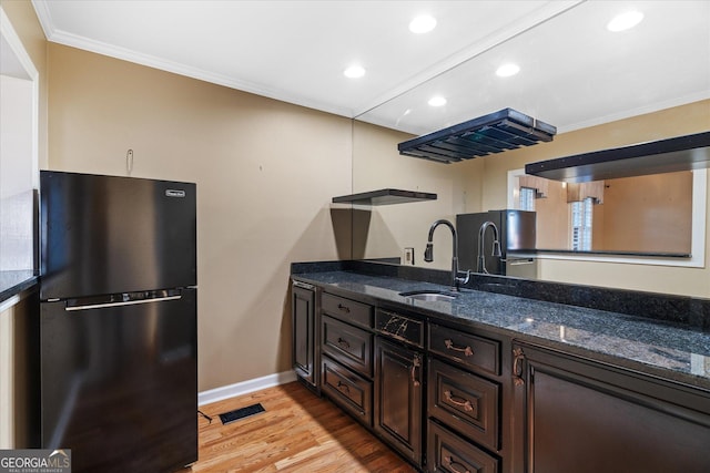 kitchen featuring dark brown cabinets, dark stone countertops, a sink, and freestanding refrigerator