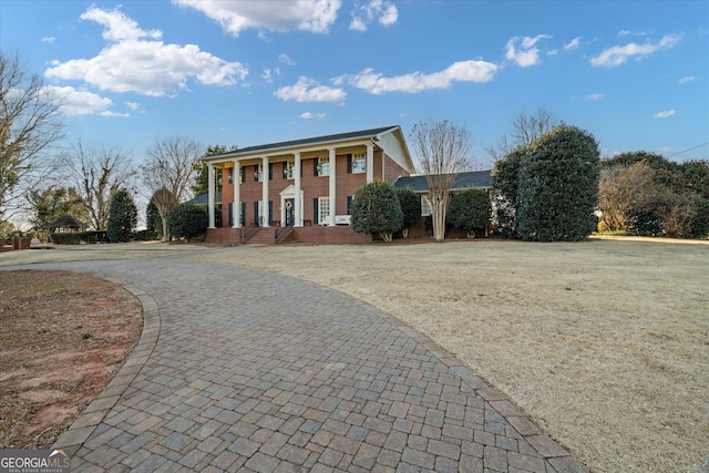 greek revival inspired property featuring a front yard, decorative driveway, and brick siding