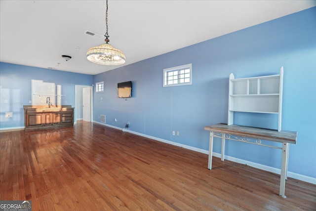 unfurnished living room featuring visible vents, a sink, baseboards, and wood finished floors