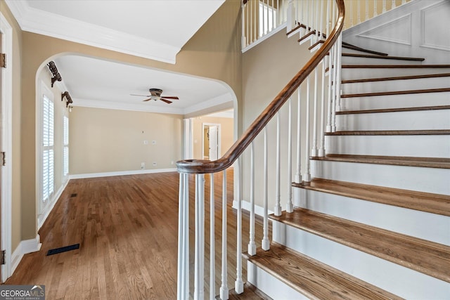 staircase featuring arched walkways, wood finished floors, visible vents, and crown molding