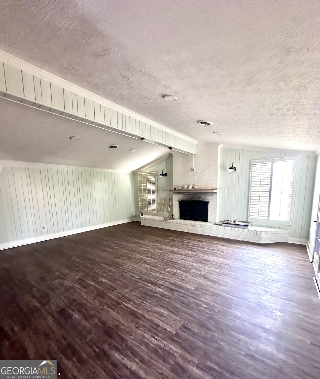 unfurnished living room with lofted ceiling, a textured ceiling, a brick fireplace, and wood finished floors