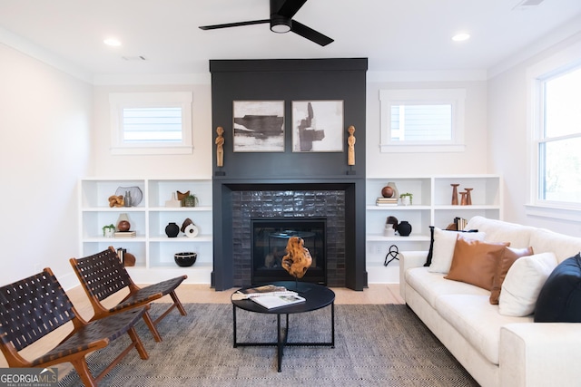 living room with ceiling fan, ornamental molding, and a tiled fireplace