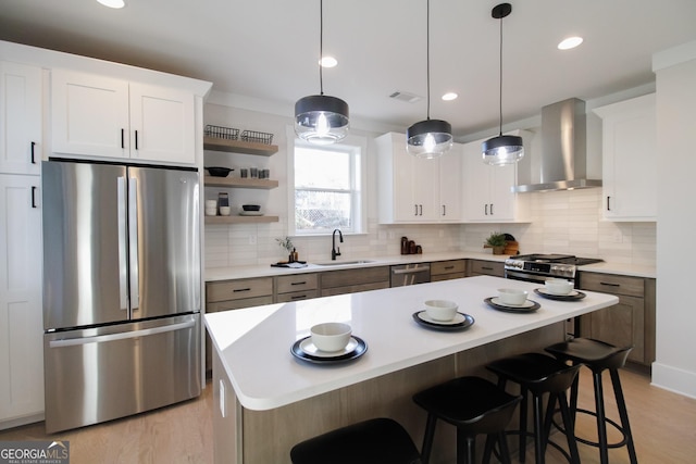 kitchen with sink, appliances with stainless steel finishes, white cabinetry, a center island, and wall chimney exhaust hood