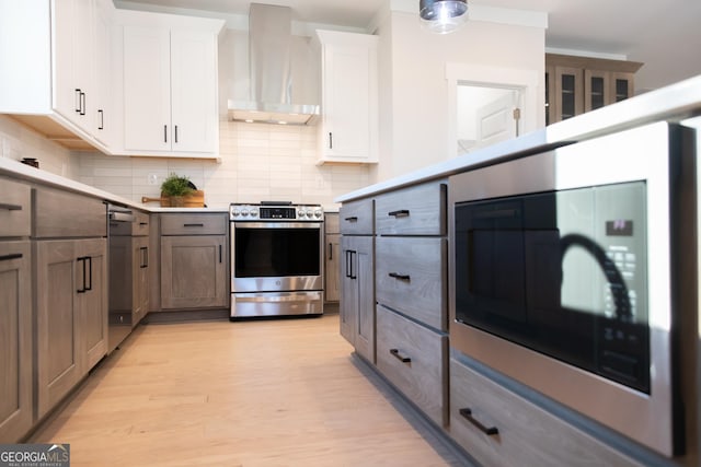 kitchen featuring white cabinetry, stainless steel appliances, backsplash, and wall chimney range hood