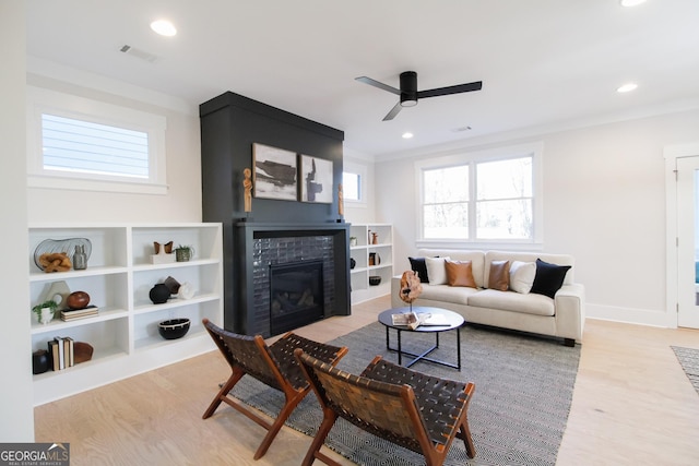 living room featuring ceiling fan, a large fireplace, and light wood-type flooring