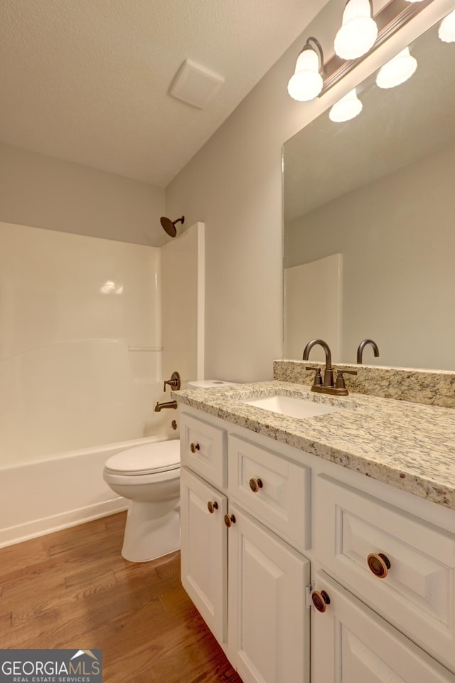 full bathroom featuring bathing tub / shower combination, hardwood / wood-style floors, vanity, a textured ceiling, and toilet