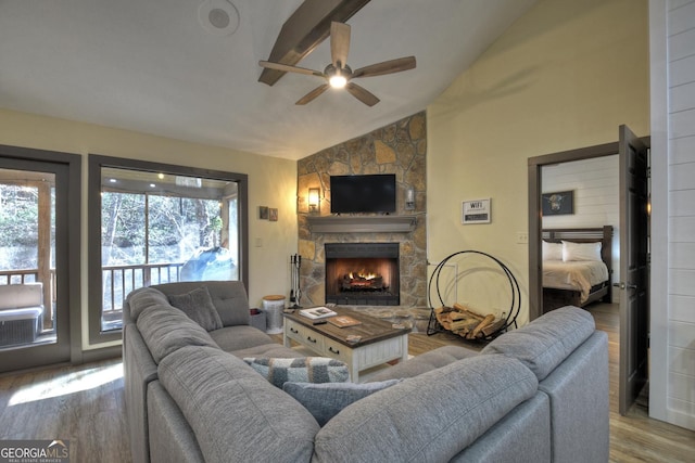 living room with hardwood / wood-style flooring, vaulted ceiling, a stone fireplace, and ceiling fan