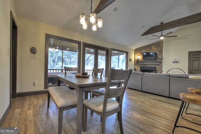 dining area with vaulted ceiling with beams, a fireplace, wood-type flooring, ceiling fan with notable chandelier, and french doors