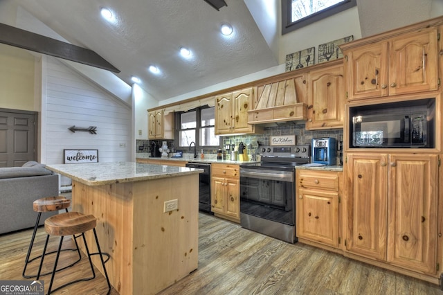 kitchen featuring premium range hood, a center island, light hardwood / wood-style floors, black appliances, and vaulted ceiling