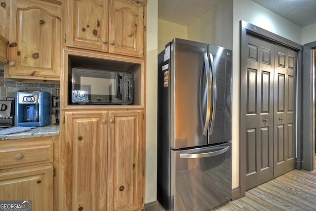 kitchen with decorative backsplash, light stone countertops, stainless steel refrigerator, and a textured ceiling