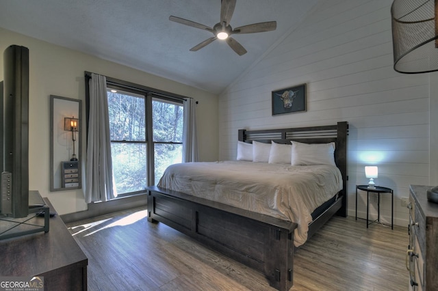 bedroom featuring ceiling fan, wood-type flooring, wooden walls, and vaulted ceiling