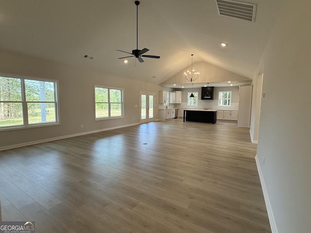 unfurnished living room featuring ceiling fan with notable chandelier, visible vents, wood finished floors, and baseboards