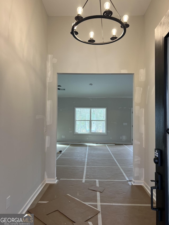 hallway featuring a towering ceiling, baseboards, and a chandelier