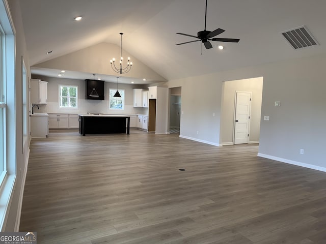 unfurnished living room featuring high vaulted ceiling, ceiling fan with notable chandelier, baseboards, visible vents, and wood finished floors