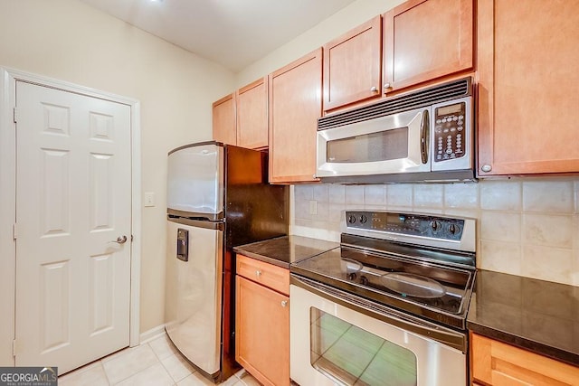 kitchen featuring light tile patterned floors, appliances with stainless steel finishes, dark countertops, and backsplash