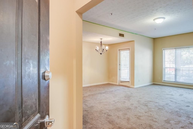 carpeted empty room with a chandelier, a textured ceiling, visible vents, and baseboards