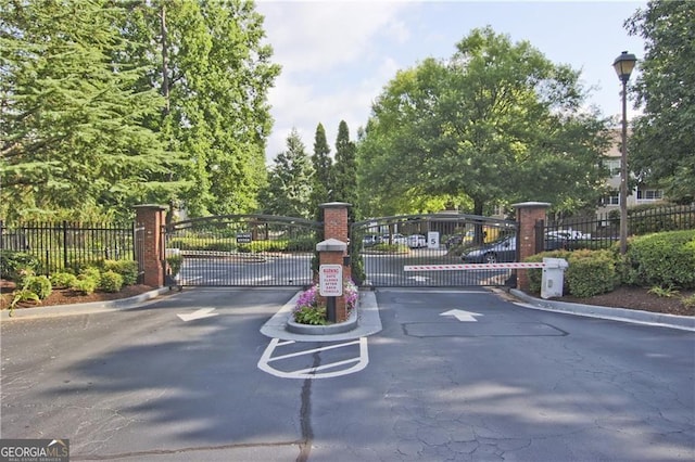 view of road with a gate, a gated entry, street lights, and curbs