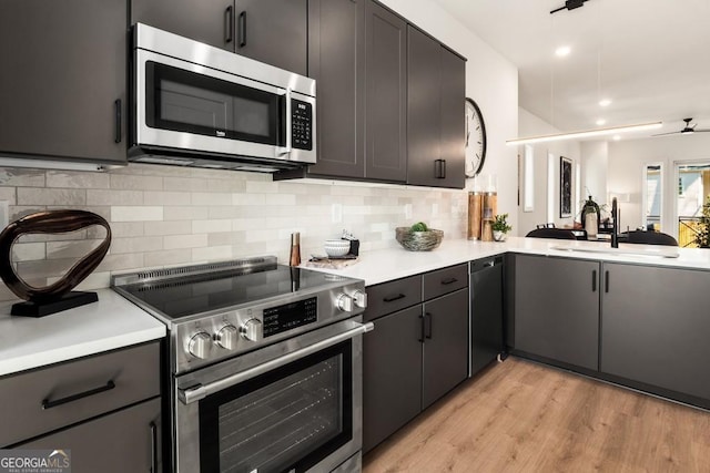 kitchen with sink, ceiling fan, appliances with stainless steel finishes, decorative backsplash, and light wood-type flooring