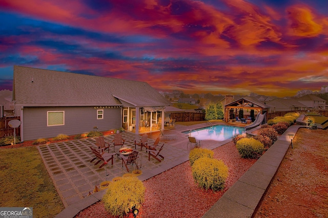 pool at dusk with a gazebo, a water slide, and a patio area