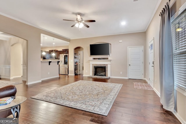 living room featuring ornamental molding, ceiling fan, a fireplace, and dark hardwood / wood-style flooring