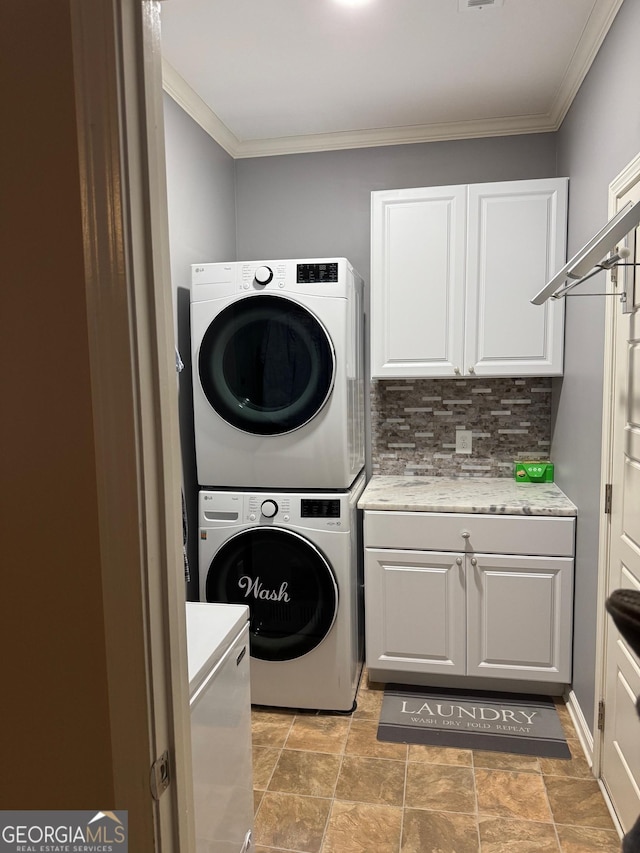 laundry area featuring crown molding, cabinets, and stacked washing maching and dryer