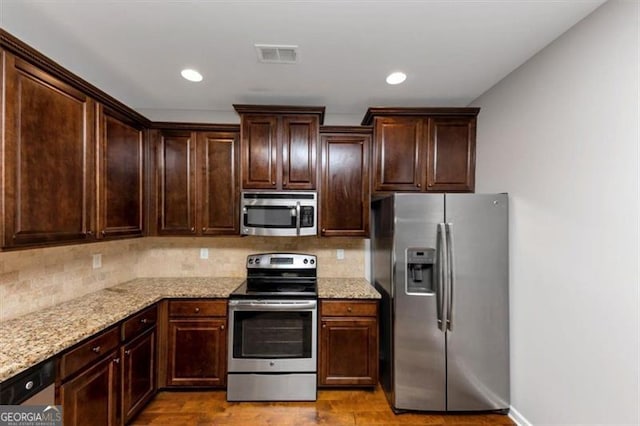 kitchen with light stone counters, decorative backsplash, light hardwood / wood-style flooring, and stainless steel appliances