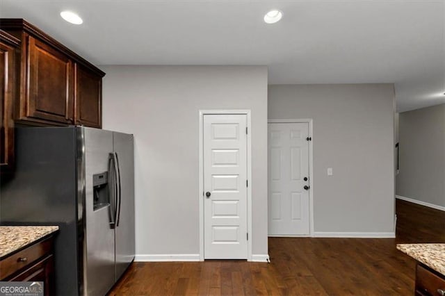 kitchen featuring light stone counters, dark brown cabinetry, dark wood-type flooring, and stainless steel fridge with ice dispenser