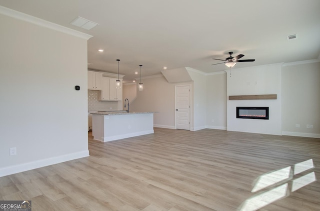 unfurnished living room featuring ceiling fan, ornamental molding, and light wood-type flooring