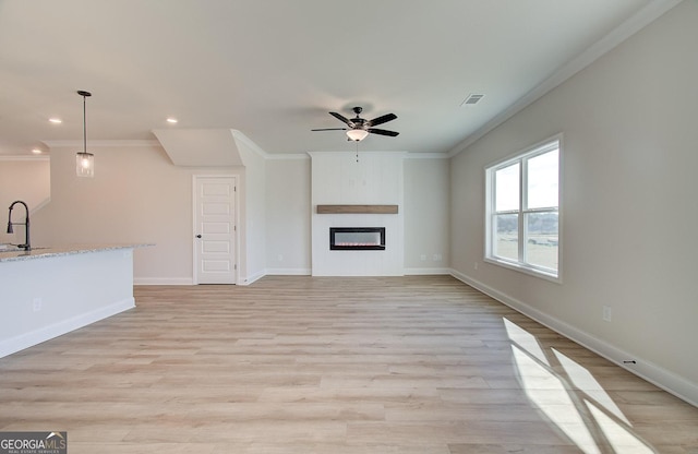 unfurnished living room featuring ceiling fan, ornamental molding, light hardwood / wood-style floors, and sink