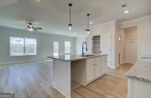 kitchen featuring pendant lighting, sink, a kitchen island with sink, white cabinets, and light wood-type flooring