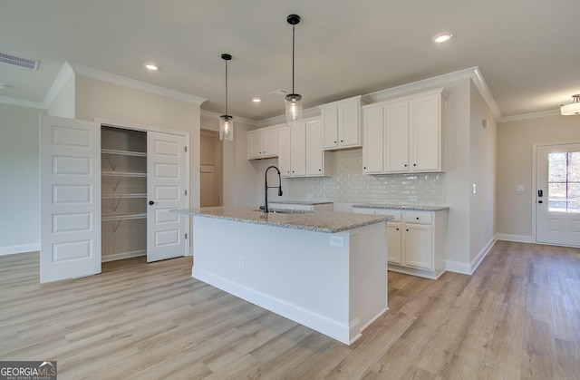 kitchen with white cabinetry, sink, hanging light fixtures, light stone counters, and a center island with sink