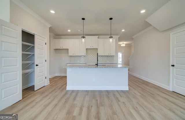 kitchen featuring hanging light fixtures, a center island with sink, light stone countertops, decorative backsplash, and white cabinets