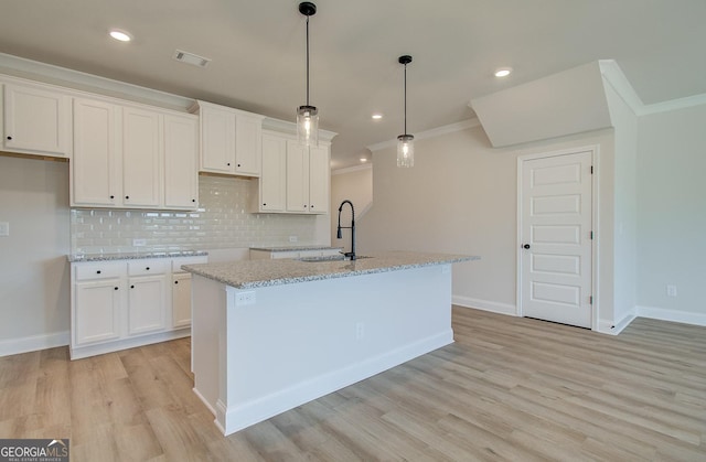 kitchen featuring hanging light fixtures, an island with sink, and white cabinets