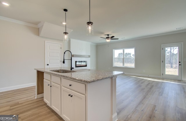 kitchen featuring pendant lighting, sink, white cabinetry, light stone countertops, and a center island with sink