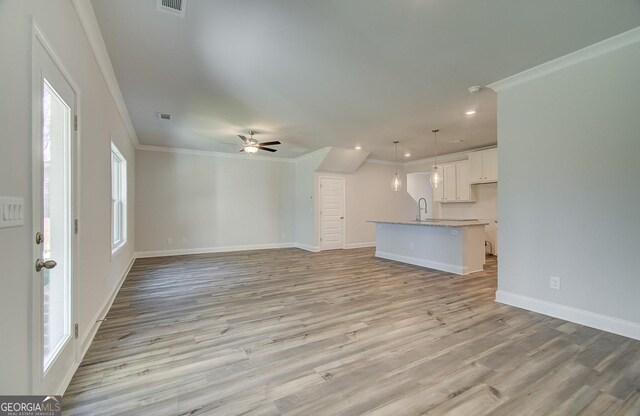 unfurnished living room with ornamental molding, sink, ceiling fan, and light wood-type flooring