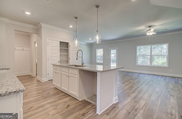 kitchen with hanging light fixtures, sink, a center island with sink, and white cabinets