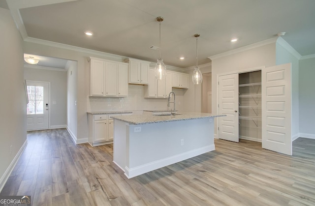 kitchen with tasteful backsplash, a center island with sink, white cabinets, and light hardwood / wood-style floors