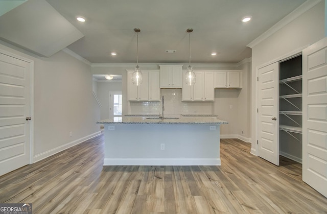 kitchen with tasteful backsplash, a center island with sink, light stone counters, and white cabinets