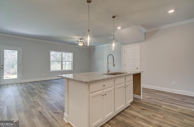 kitchen with crown molding, white cabinetry, a kitchen island with sink, and sink