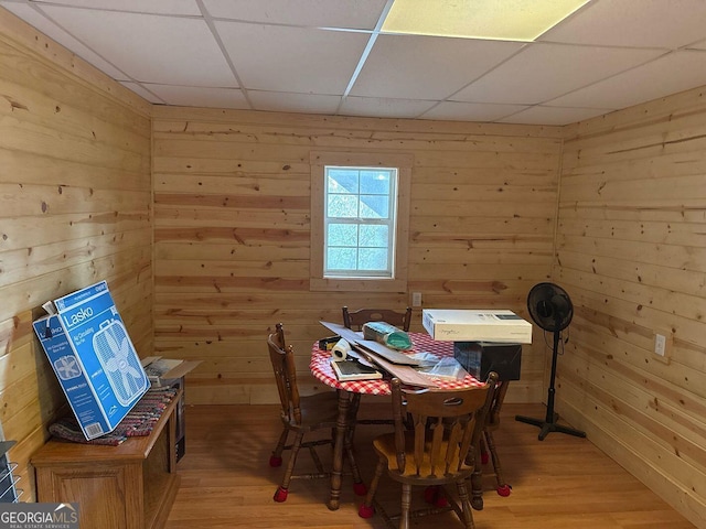 dining room with hardwood / wood-style flooring, a paneled ceiling, and wooden walls