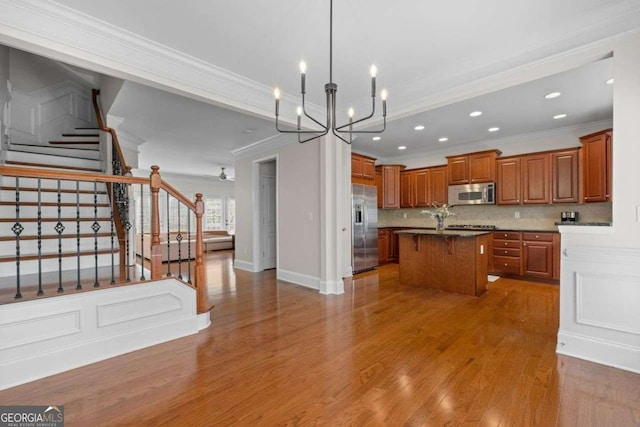 kitchen featuring appliances with stainless steel finishes, an island with sink, wood-type flooring, backsplash, and crown molding