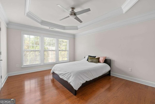 bedroom with crown molding, ceiling fan, a raised ceiling, and hardwood / wood-style floors