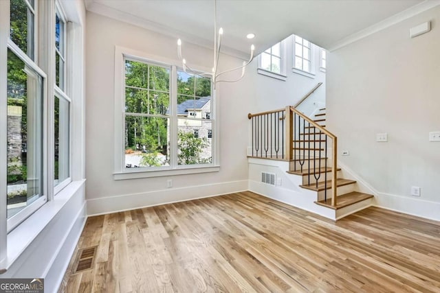 interior space featuring an inviting chandelier, plenty of natural light, ornamental molding, and light wood-type flooring